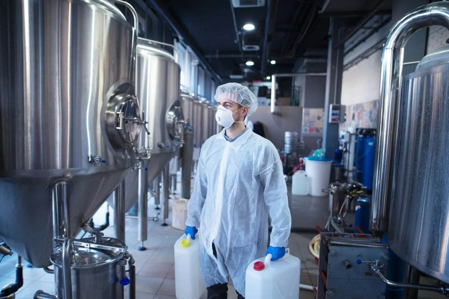 Un técnico industrial sostiene recipientes de plástico a punto de cambiar los productos químicos en la máquina procesadora de alimentos